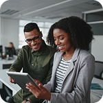 Two coworkers look at a tablet computer inside an office